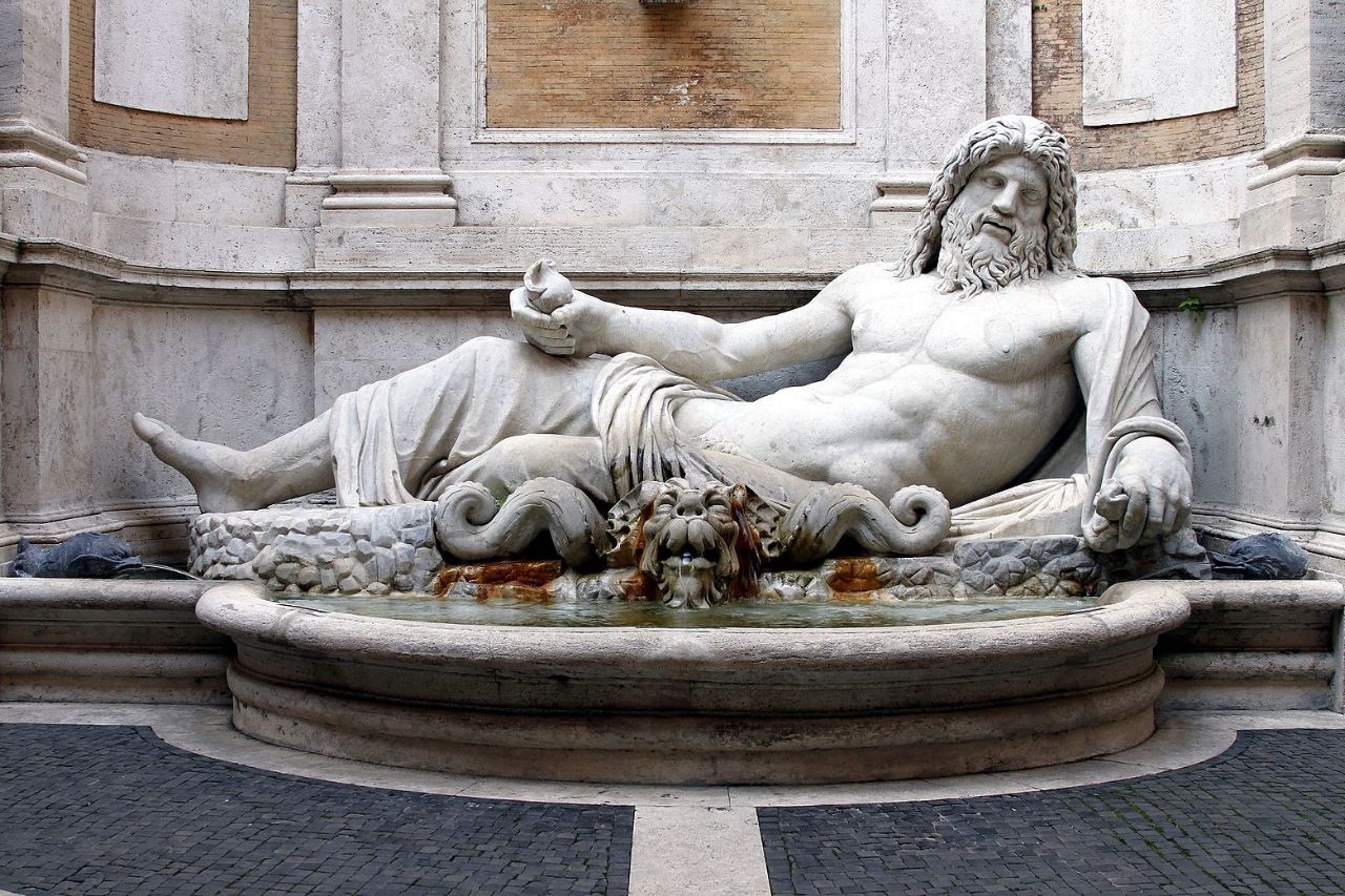 A statue of man laying over the rocks with animals on his bottom and water.