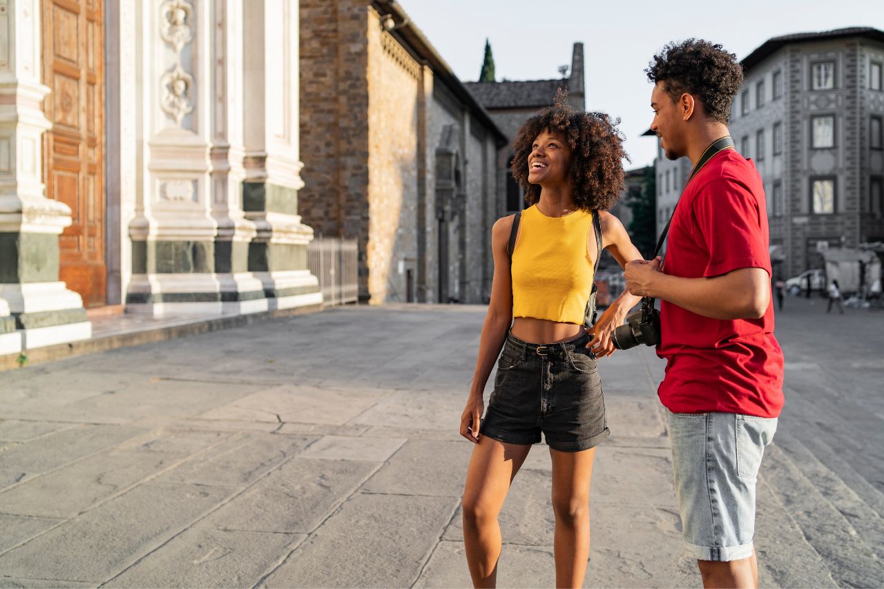 Two tourists, with summer attire, visit Florence taking pictures with a camera.