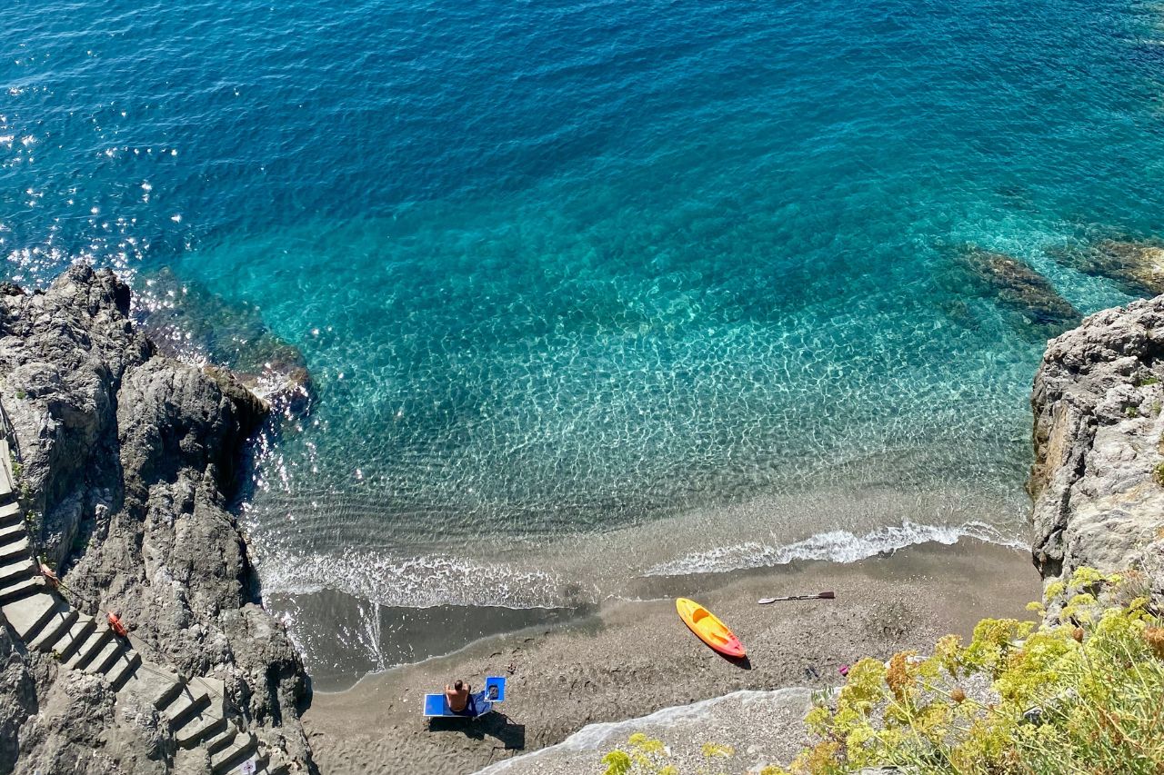A tourist enjoys watching waves on the beach with clear water in Positano.