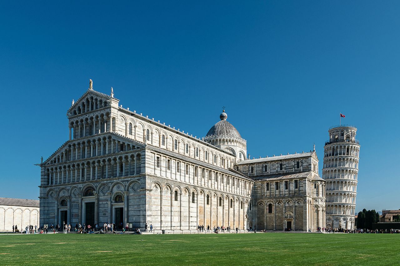 Iconic Leaning Tower of Pisa and surrounding architectural ensemble in Pisa, Italy, set against a blue sky backdrop.