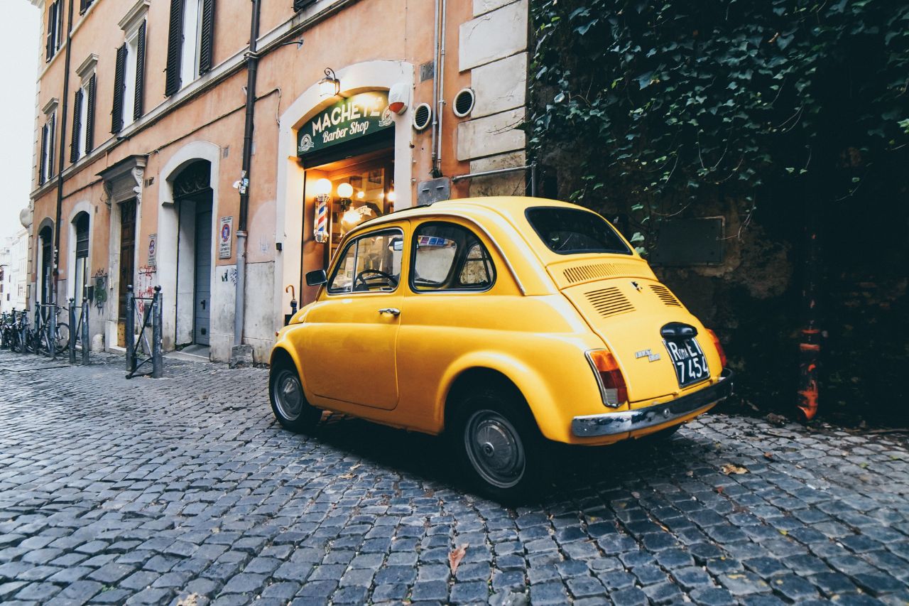 The Fiat 500 is a historic Italian car parked in front of a barber shop in Tuscan.