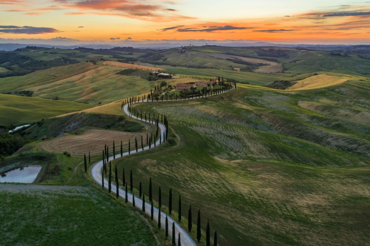 An aerial view of a zigzag road with a beautiful sunset in the Tuscan countryside.
