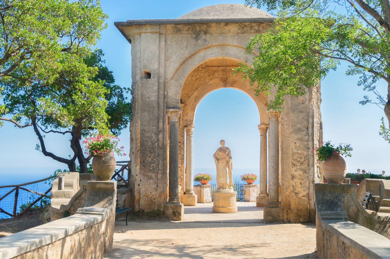 A statue in the middle of an old structure with an overlooking view of the sea and restaurants in Ravello.