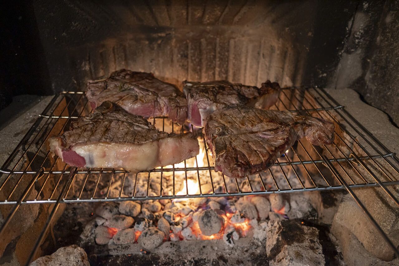 A Florentine steak being grilled outdoor by a Tuscan chef