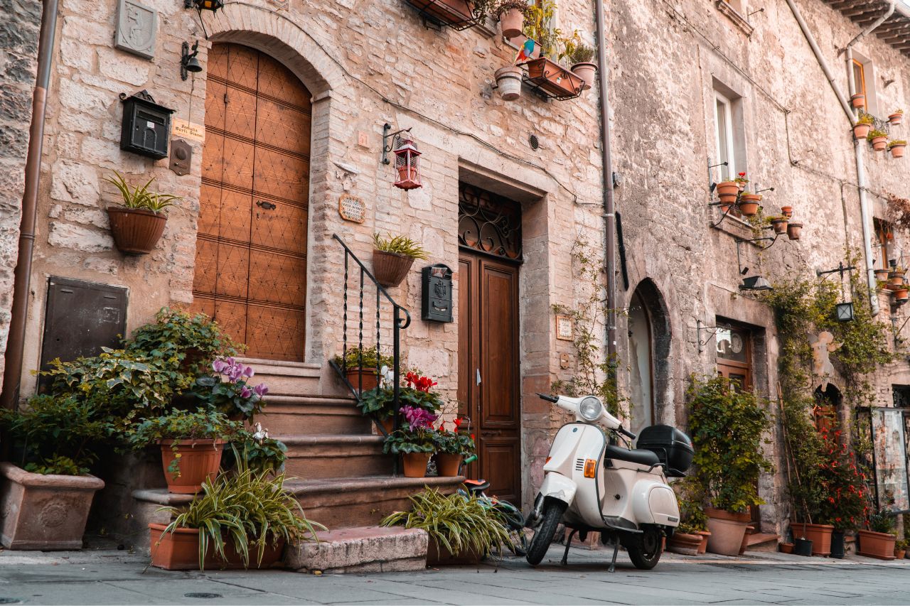 A white Vespa parked in front of old house in Tuscany.