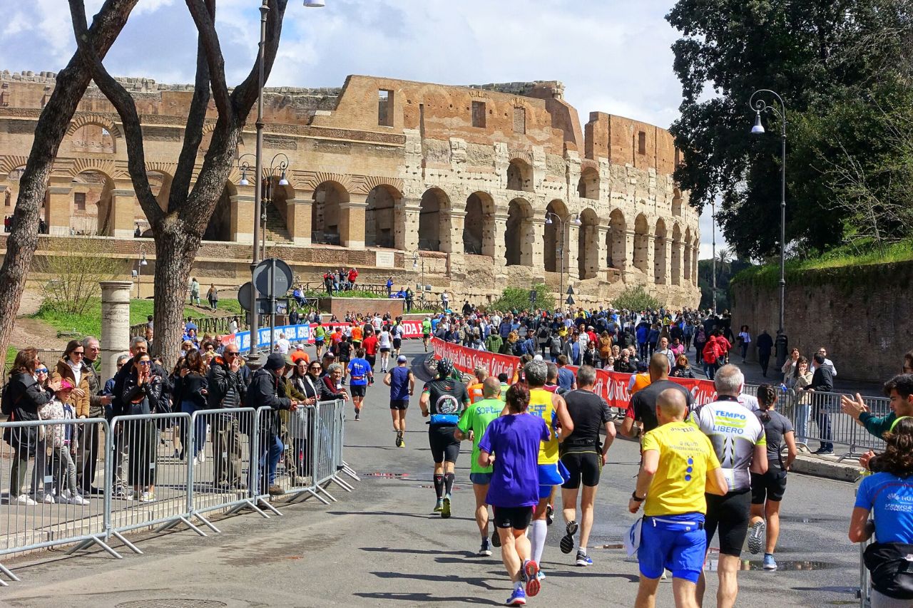 The participants of a marathon are running in front of a historical structure in Rome during winter.
