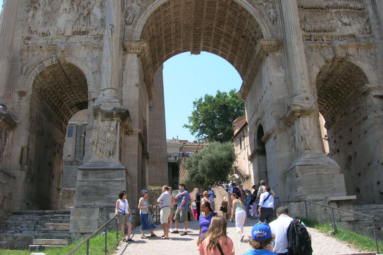 Tourists are passing through the Arch of Septimius Severus, in Rome
