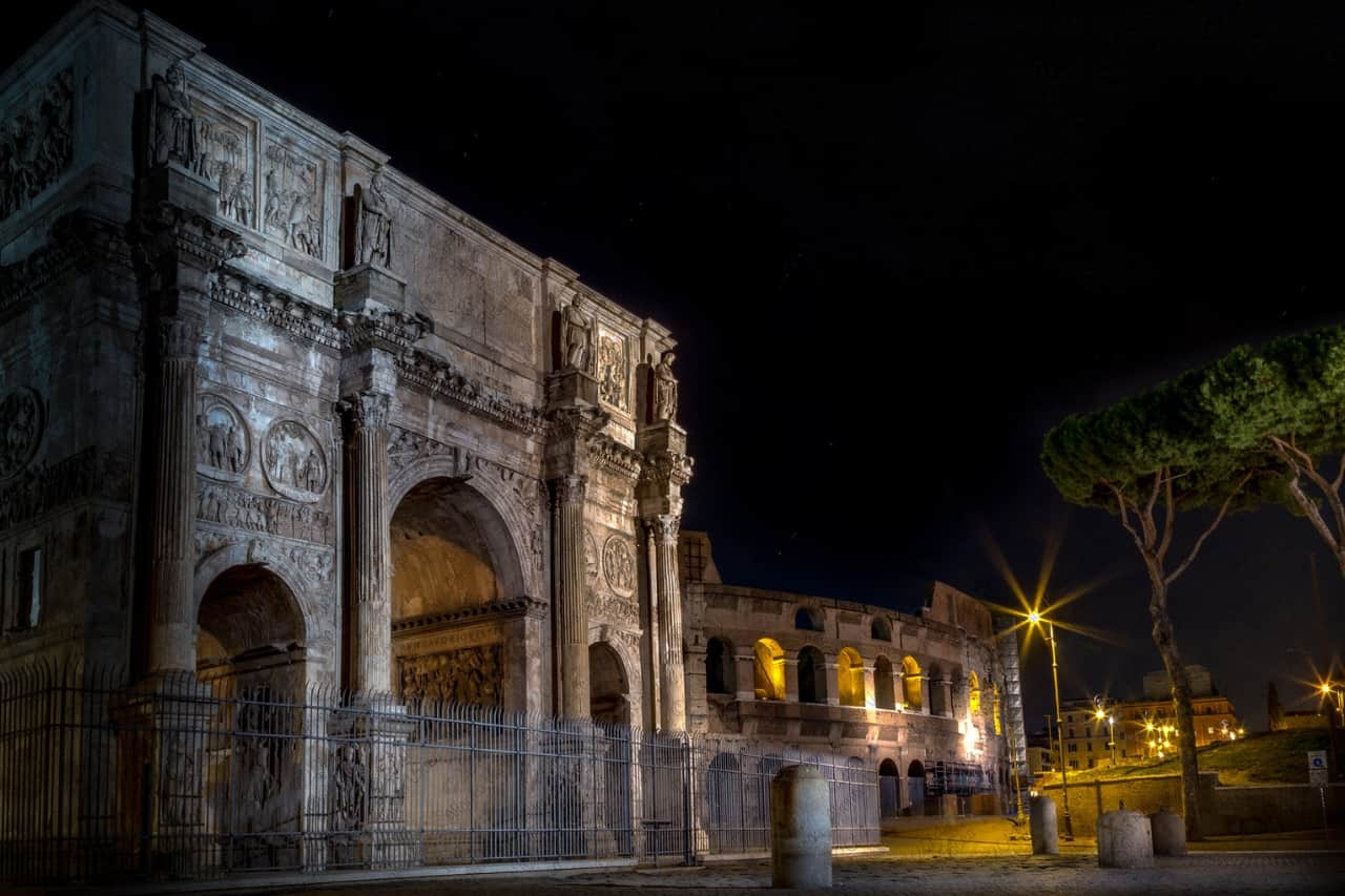 Tourists are exploring the Arch of Constantine at night: one of the most beautiful monuments in Rome